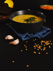 Red lentil soup, spices, herbs, vegetables, lemon and cream. Soup on a blue napkin, next to brown bread, garlic, a bowl with lentils. Lentil seeds are scattered in the foreground. Close-up.