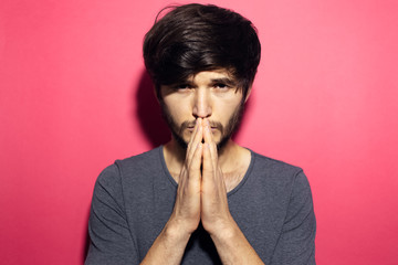 Portrait of young man praying on background of coral pink.