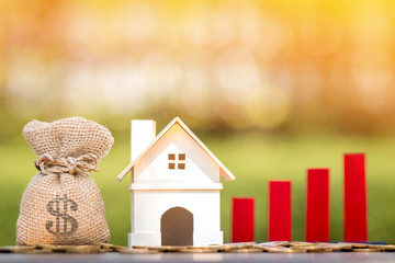 Money bag and home and red bar graph with growing value put on the coin on bokeh background in the public park, for currency and financial business investment and fund real estate concept.