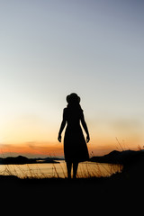 Silhouette of a woman from her back standing on a mountain at sunset in orange hues. The concept of confidence, peace and thoughts about the future