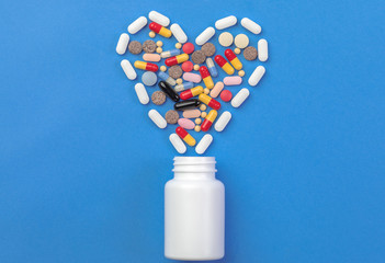 A heart shape of medicine pills pouring out of white bottle on blue background. Pharmacy and medicine concept.