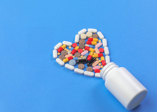 A heart shape of medicine pills pouring out of white bottle on blue background. Pharmacy and medicine concept.