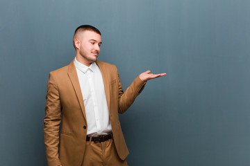 young handsome businessman feeling happy and smiling casually, looking to an object or concept held...