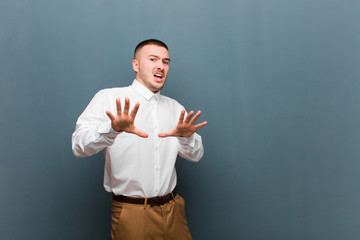 young handsome businessman feeling terrified, backing off and screaming in horror and panic,...