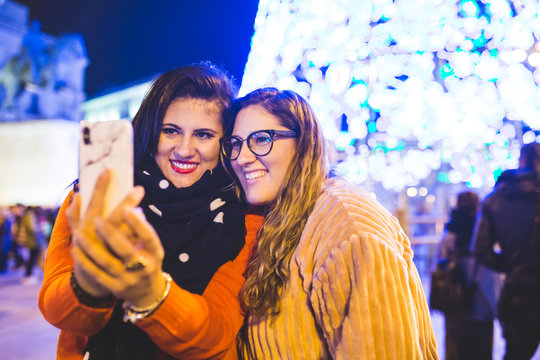 Two girls are taking a picture next to the Christmas lights. They are enjoying together in the city of Madrid.