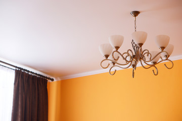 A wrought-iron vintage retro chandelier with eight shades hangs in the room, on the ceiling, not far from the window