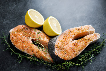 Fresh salmon steaks lie on a dark background, alongside lemon and rosemary. Top view