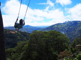 A young man sitting on a large wooden swing at the treehouse under a beautiful sky, La casa del Arbol (La Casa del Árbol), Banos (Baños), Ecuador