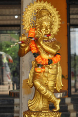 Golden Color Plaster Of Paris Statue Of Lord God Krishna Playing Flute and Wearing Yellow Colored Flower Garland
