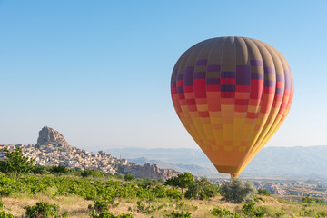 One hot air balloon flying low over the field. Uchisar castle on background, Cappdocia, Turkey.