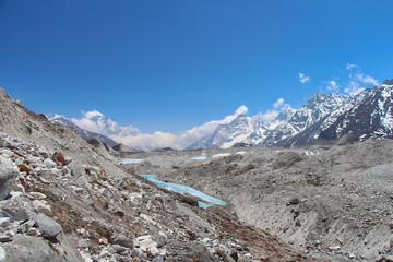 View of Ngozumpa glacier covered with stones in Himalayas in Nepal at an altitude of about 5000 meters. The glacier is surrounded by mountains, and lakes of melted ice are visible on its surface.