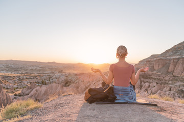 Back view of young woman sitting on the edge of canyon and meditating. Yoga concept. Cappadocia, sunset.