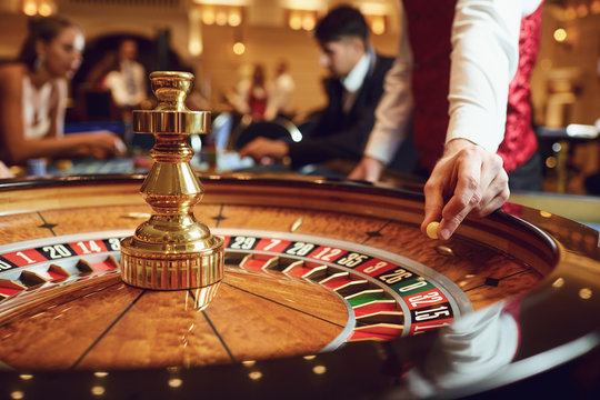 Hand of a croupier with a ball on a roulette wheel during a game in a casino.