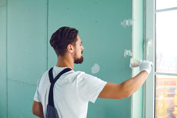 Worker builder plasterer plastering a wall of drywall at a construction site indoors