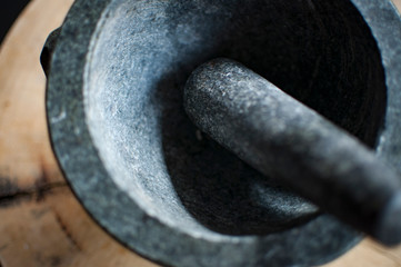 Granite stone mortar and pestle on round thick cut rustic wooden board and granite counter.