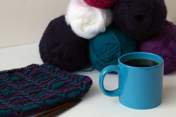 blue cup of black coffee with colour balls of wool yarn and knitting on white background
