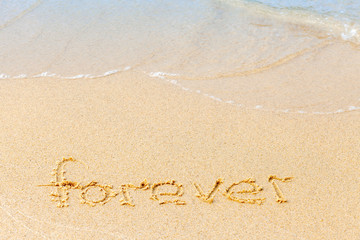Text on a sunny beach. The word Forever written by hand in the sand, washed away by the sea wave. The concept of irony and transience of life. Copy space.