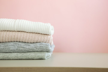 a stack of warm sweaters on the table on a colored background.