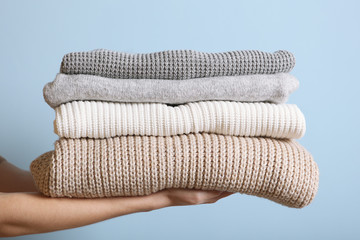 A stack of sweaters in female hands on a colored background. Warm clothes.