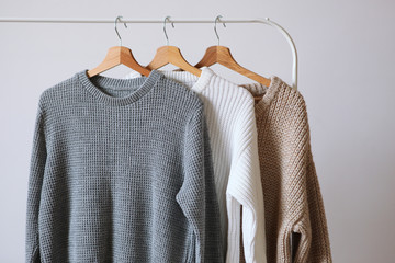 Warm sweaters on a wardrobe hanger on a light background. Autumn, winter clothes.