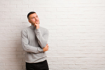 young handsome man thinking, feeling doubtful and confused, with different options, wondering which...