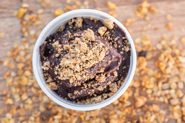 Acai in cup with peanut candy on wooden background with granola