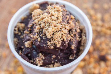 Acai in cup with peanut candy on wooden background with granola
