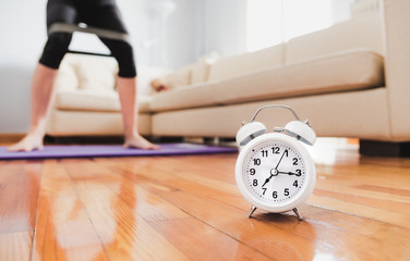 White classic alarm clock on wooden florr and unfocused young woman with fitness band on background...