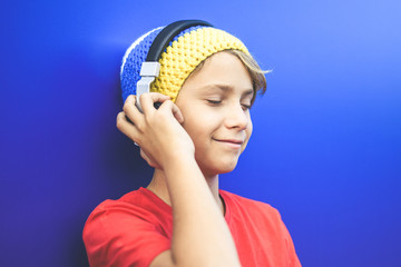 Portrait of a smiling beautiful boy listening music with headphones isolated on a blue background....