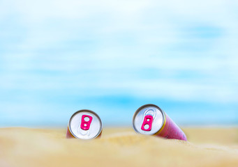 Two pink cans on sand with blue sea at background. Selective focus, blurred background.