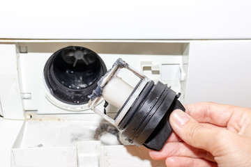 Inspecting washing machine's dirty clogged drain pump filter close up, clean and repair