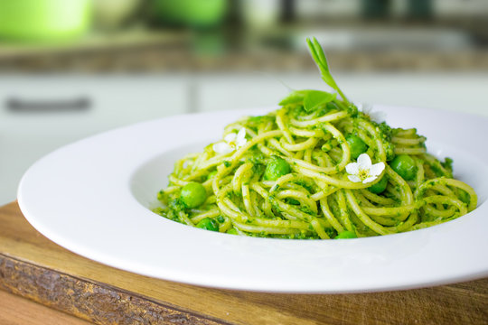 Food photography of spaghetti with a bright green wild garlic pesto, peas and flowers