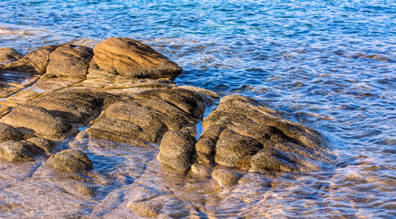 rocky shore line scenic view waterfront blue water with evening orange lighting on stones surface 