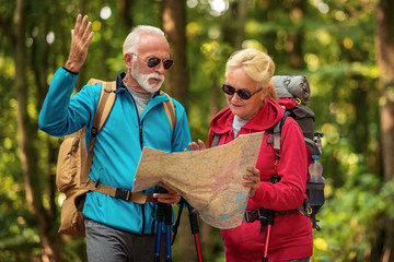 Senior couple of tourists looking at map in forest