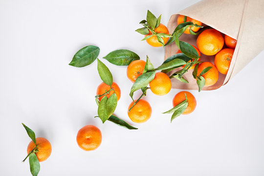 Christmas fruit. Orange fresh tangerines or mandarines with green leaves in a paper bag lie on a white background. - Powered by Adobe