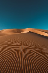 Vertical shot of a peaceful desert under the clear blue sky captured in Morocco - obrazy, fototapety, plakaty