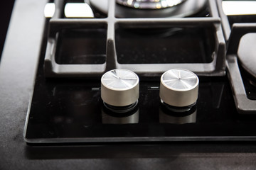 Obraz na płótnie Canvas gas stove burner knobs with black mirror surface of cooker and stainless steel grills. top view, close up