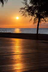 Fototapeta na wymiar Orange sun rising above the sea. View from promenade with the sea, beach and cafe. The solar path is reflected from pedestrian zone made of wood.