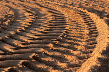 Car tyre prints on wet sea sand during the day, selective focus. Traces of car or tractor tires on the sand of the sea beach.
