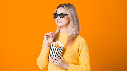 Young cheerful woman in 3D glasses watching a movie and eating popcorn.