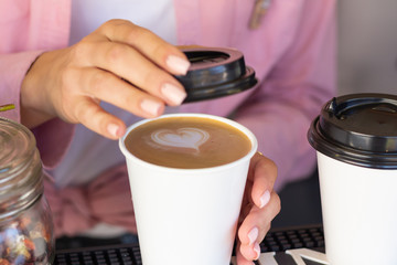 Barista woman closes a mug with a coffee lid. Cappuccino with a heart-shaped pattern. Closeup