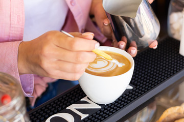 Barista girl pouring steamed milk from a pitcher into a cup of coffee, making a beautiful bear pattern.  Latte art close-up