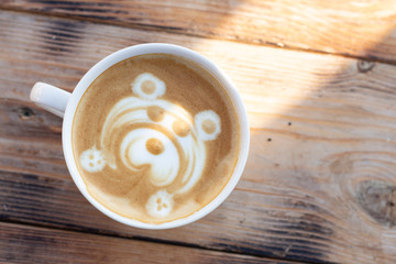 Cup of cappuccino on a wooden table. Coffee with milk foam and a bear pattern. Sunlight in mug.