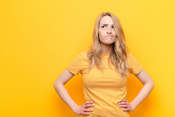young pretty blonde woman looking puzzled and confused, wondering or trying to solve a problem or...