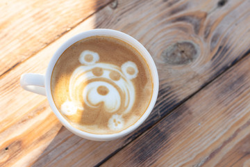 Sunlight in cup of coffee on a wooden table. Cappuccino with a bear pattern. Top view