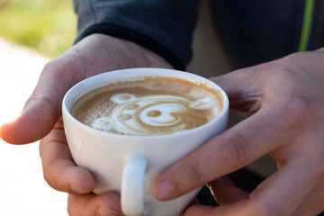 A mug of morning coffee in the hands of a man. Cappuccino with a bear pattern