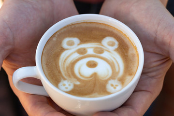 A man holds a mug of coffee. Cappuccino with a pattern of a bear made of milk foam. Close-up.