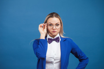 businesswoman in a stylish blue jacket and bow tie adjusts her glasses.