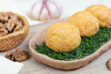 Cheese balls with carrots and walnuts. Tasty appetizer on a clay plate with dill. Close-up.