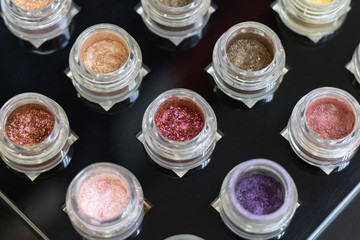 Jars with multi-colored eye shadows on a black background. Shiny eye shadow